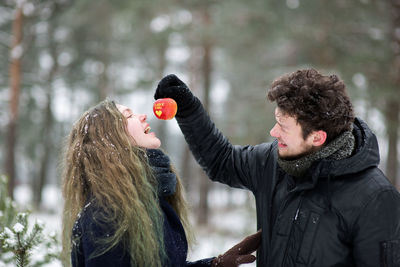 Young couple eating apple in forest during winter