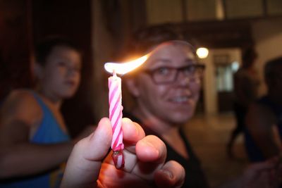 Cropped hand holding lit candle with family in background