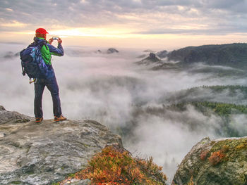 Fall nature within misty morning. photographer taking picture of forest, sky and clouds