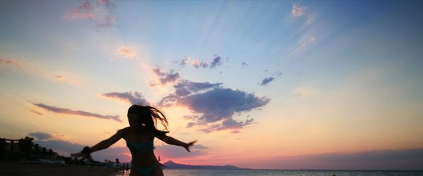 Silhouette woman with arms outstretched standing against sea during sunset