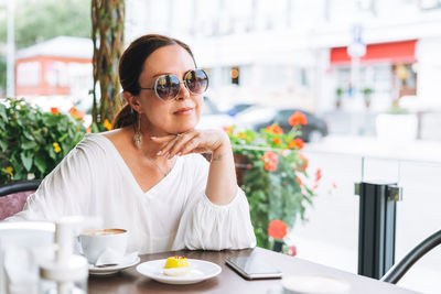 Portrait of smiling beautiful brunette middle aged woman with coffee at terrace of summer cafe