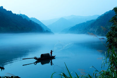 Man fishing in lake against sky