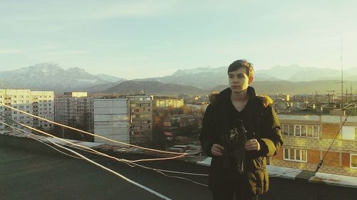 Portrait of man standing by railing in city against sky