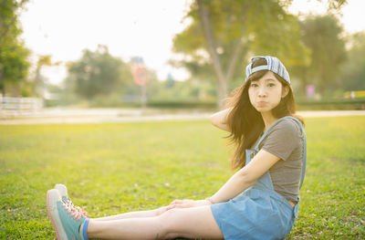 Full length portrait of young woman sitting on field at park