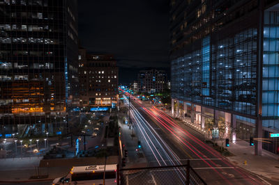 Light trails on city street amidst buildings at night