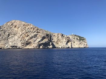 Scenic view of rock by sea against clear blue sky