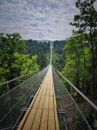 Footbridge amidst trees in forest against sky