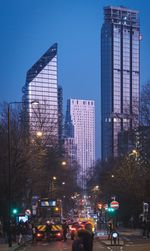 Cars on illuminated street by buildings against sky at night