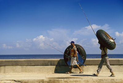 People fishing on beach against blue sky