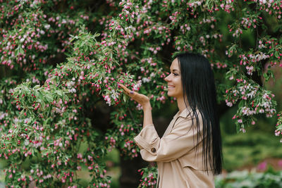 Caucasian young brunette woman sniffs the flowers of an ornamental apple tree in spring in the park