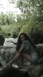 Young woman sitting on rock by trees in forest