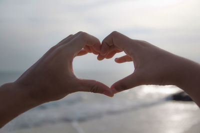 Cropped image of woman hand holding heart shape against sky