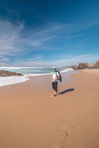 Rear view of woman walking at beach against sky