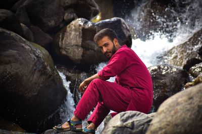 Side view portrait of young man sitting on rock