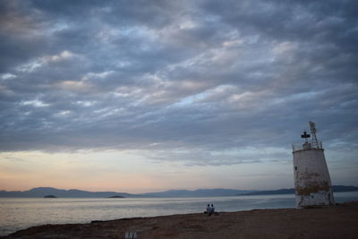Lighthouse on shore against cloudy sky