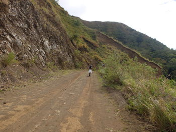 Rear view of man walking on road against sky
