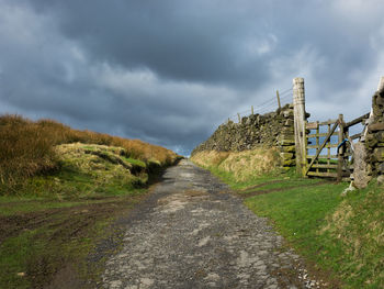 Footpath on field against cloudy sky