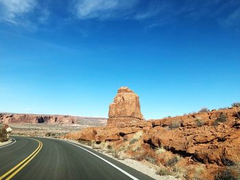 Rock formations on road against blue sky