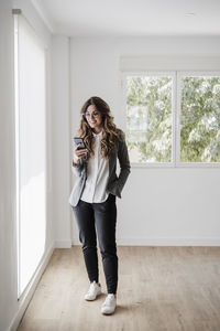 Young businesswoman standing in office using smartphone