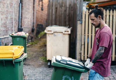 Side view of man holding garbage bin standing on street