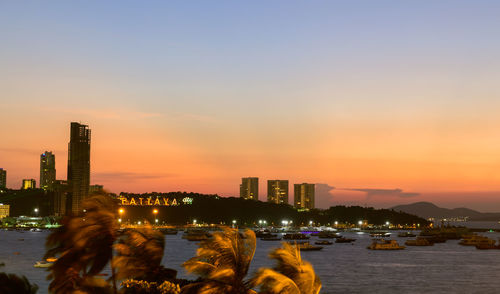 Illuminated buildings by sea against sky during sunset