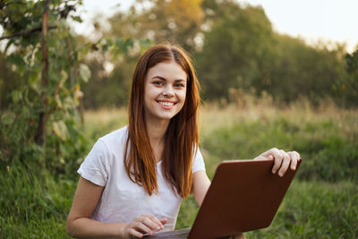 Portrait of young woman using laptop while sitting on field