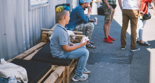 Rear view of man holding cigarette while sitting on street