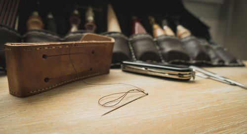 Close-up of penknife with leather and sewing needle on table