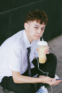 Portrait of young man drinking drink sitting outdoors