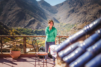 Portrait of young woman standing on table against mountains