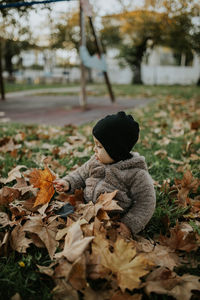 Rear view of boy on dry leaves on field