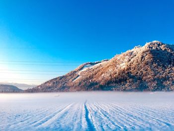 Snow covered landscape against clear blue sky