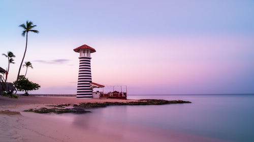 Lighthouse by sea against sky during sunset