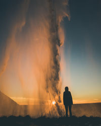 Silhouette people standing next to waterfall at sunset