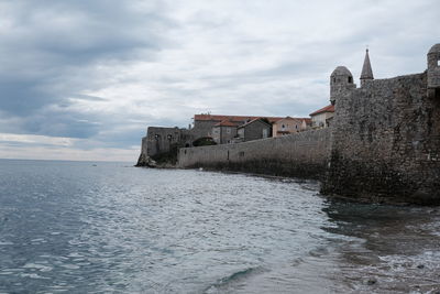 Old building by sea against cloudy sky