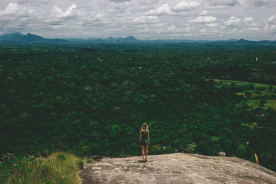 Rear view of young woman standing on mountain against cloudy sky