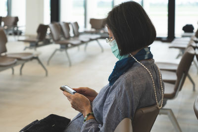 Woman wearing mask using mobile phone while sitting on chair