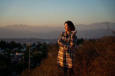 Woman standing on field against sky during sunset