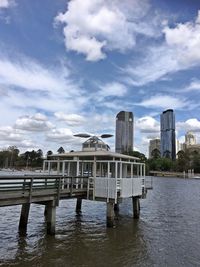 Pier over river by buildings against sky