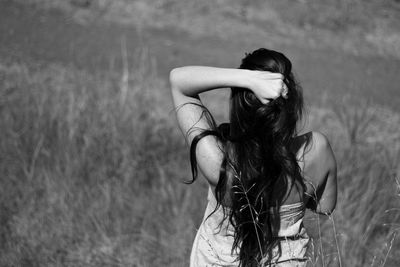 Rear view of woman with hand in hair standing on grassy field