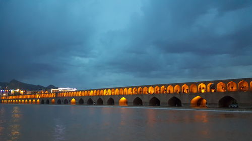 Arch bridge over river against sky at dusk