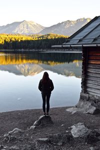 Rear view of woman standing on rock while looking at lake against sky