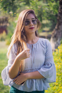 Beautiful young woman wearing sunglasses standing against plants