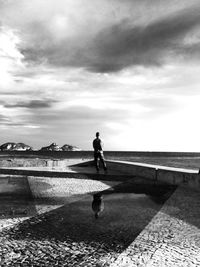 Woman standing by sea against cloudy sky