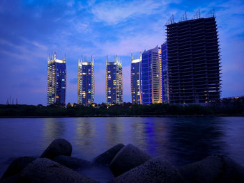 River by illuminated buildings against sky at dusk