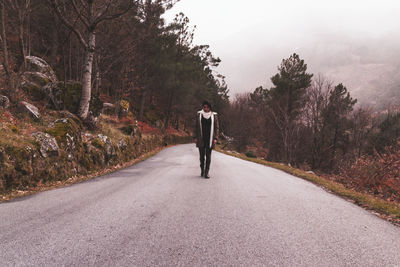 Woman walking on road amidst plants against sky