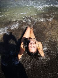 High angle view of woman sitting in splashing water at shore