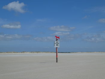 Road sign on beach against blue sky
