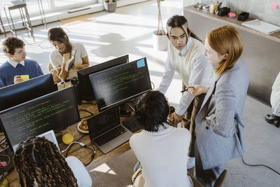 Businesswoman discussing with male and female programmers at desk in startup office