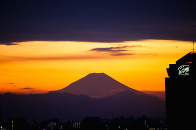 Silhouette buildings and mountains against romantic sky at sunset